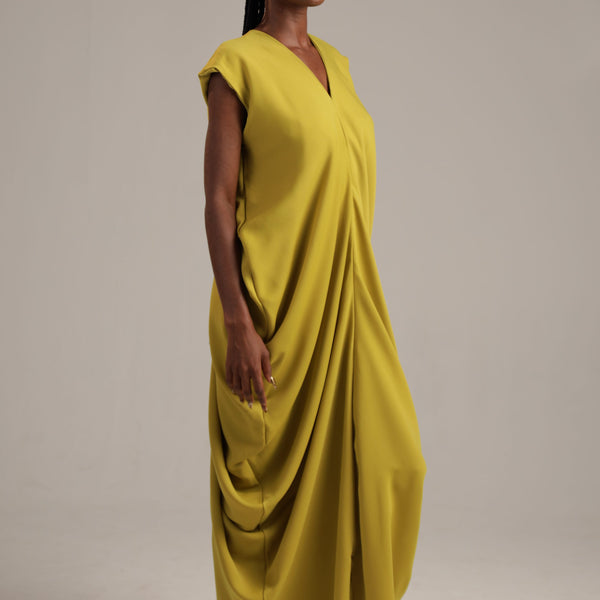 Woman wearing a yellow draped dress against a plain background