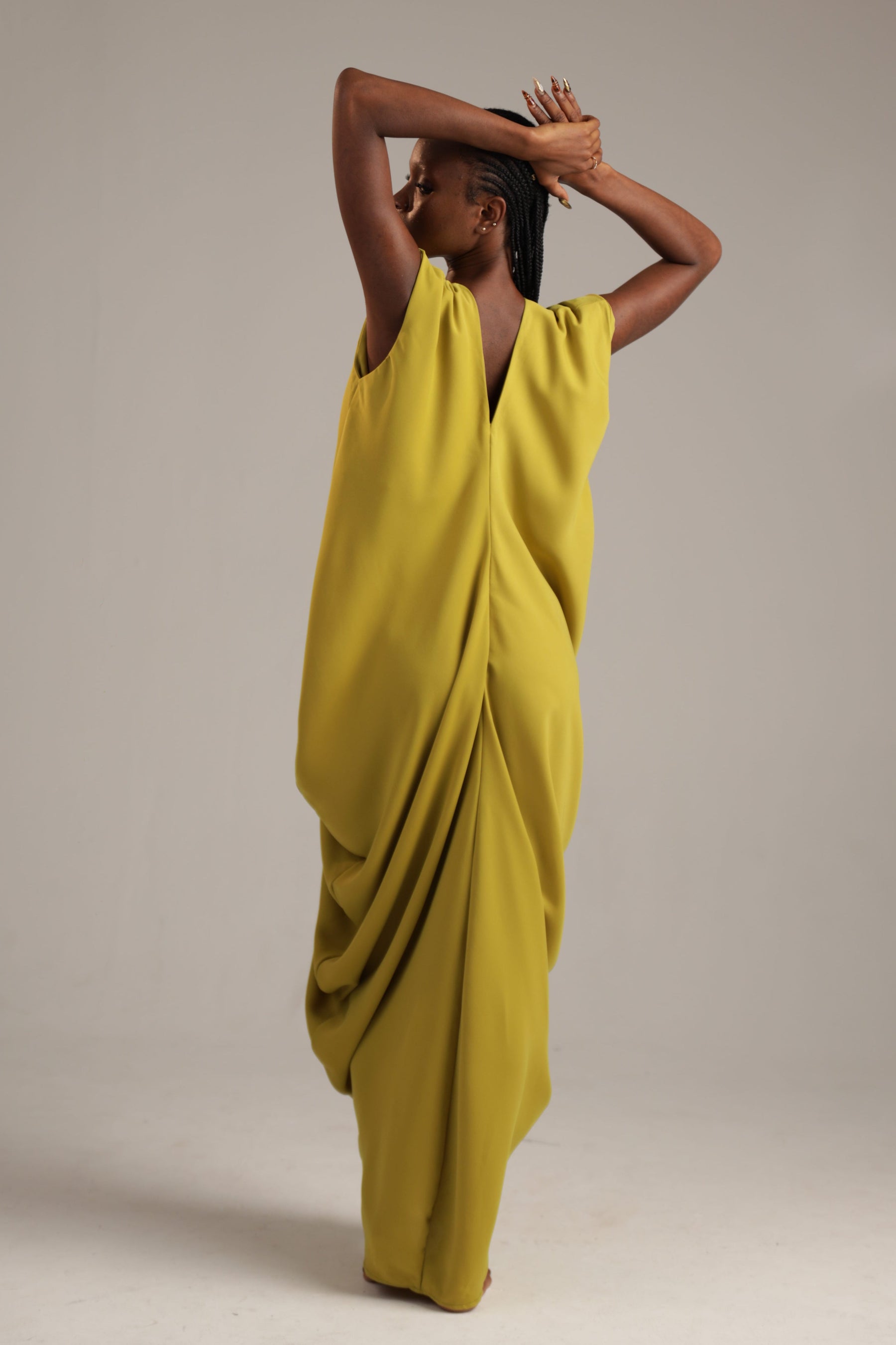 Woman wearing a yellow draped dress against a plain background