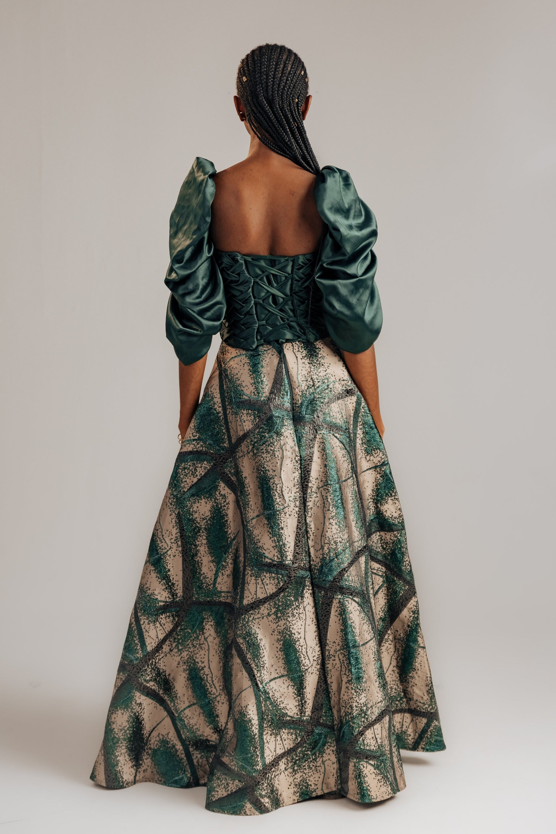 Woman wearing a green and beige patterned dress with puff sleeves on a plain background