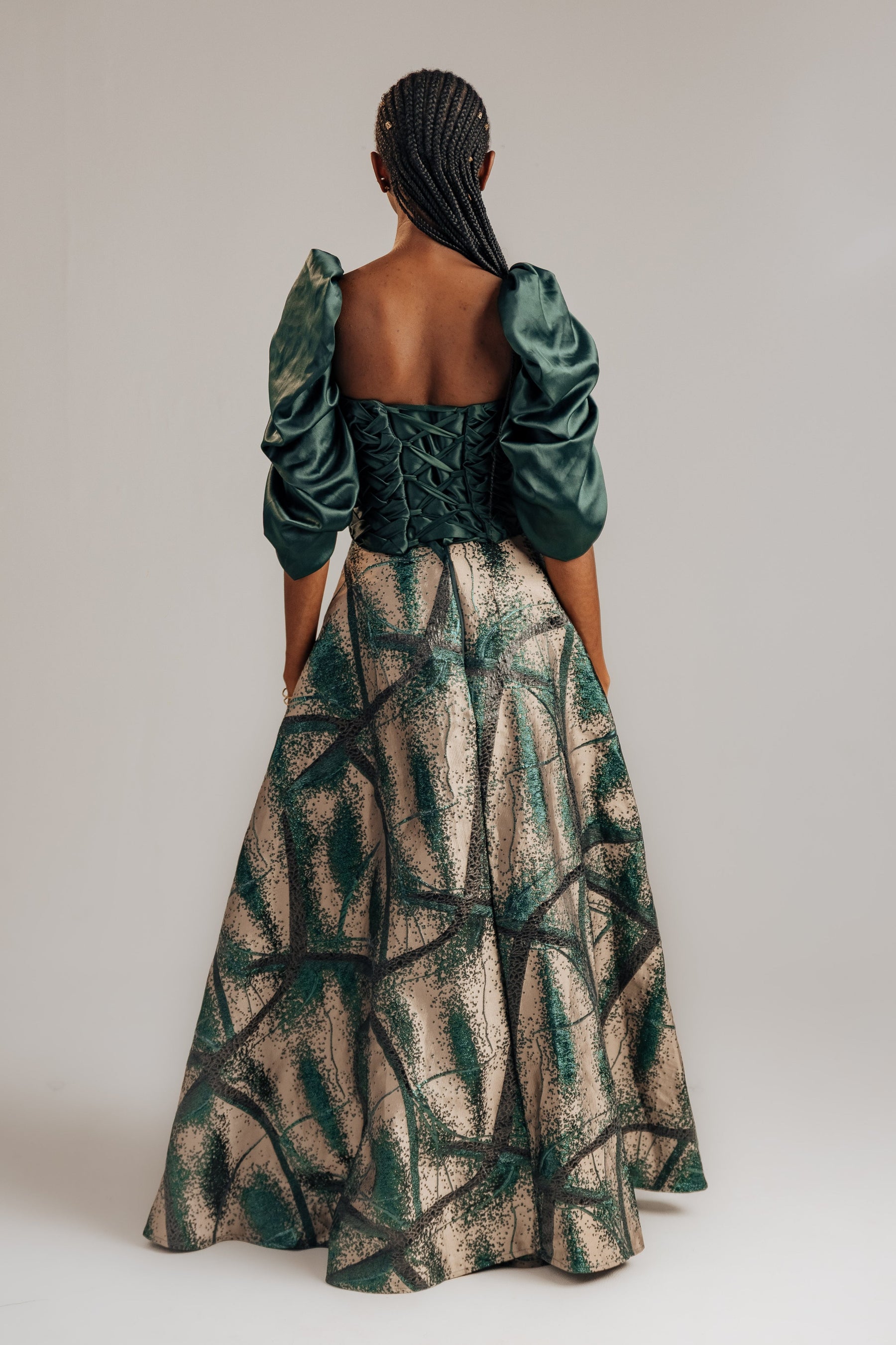 Woman wearing a green and beige patterned dress with puff sleeves on a plain background