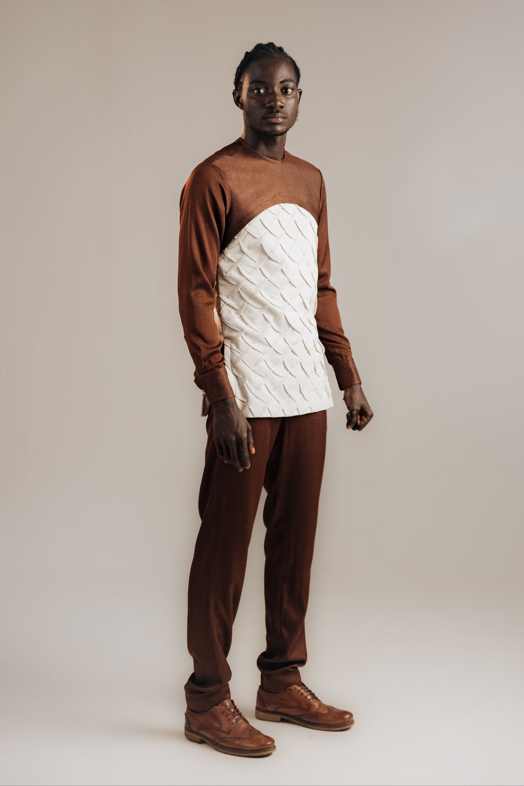 Person wearing a brown and white sweater with brown pants on a plain background