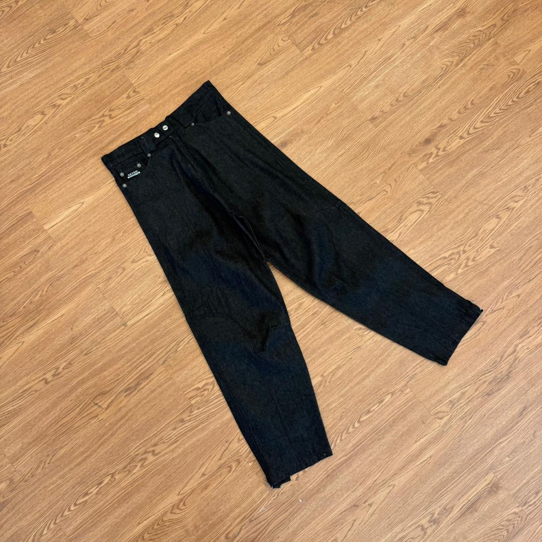 Black denim jeans laid flat on a light brown wooden floor.