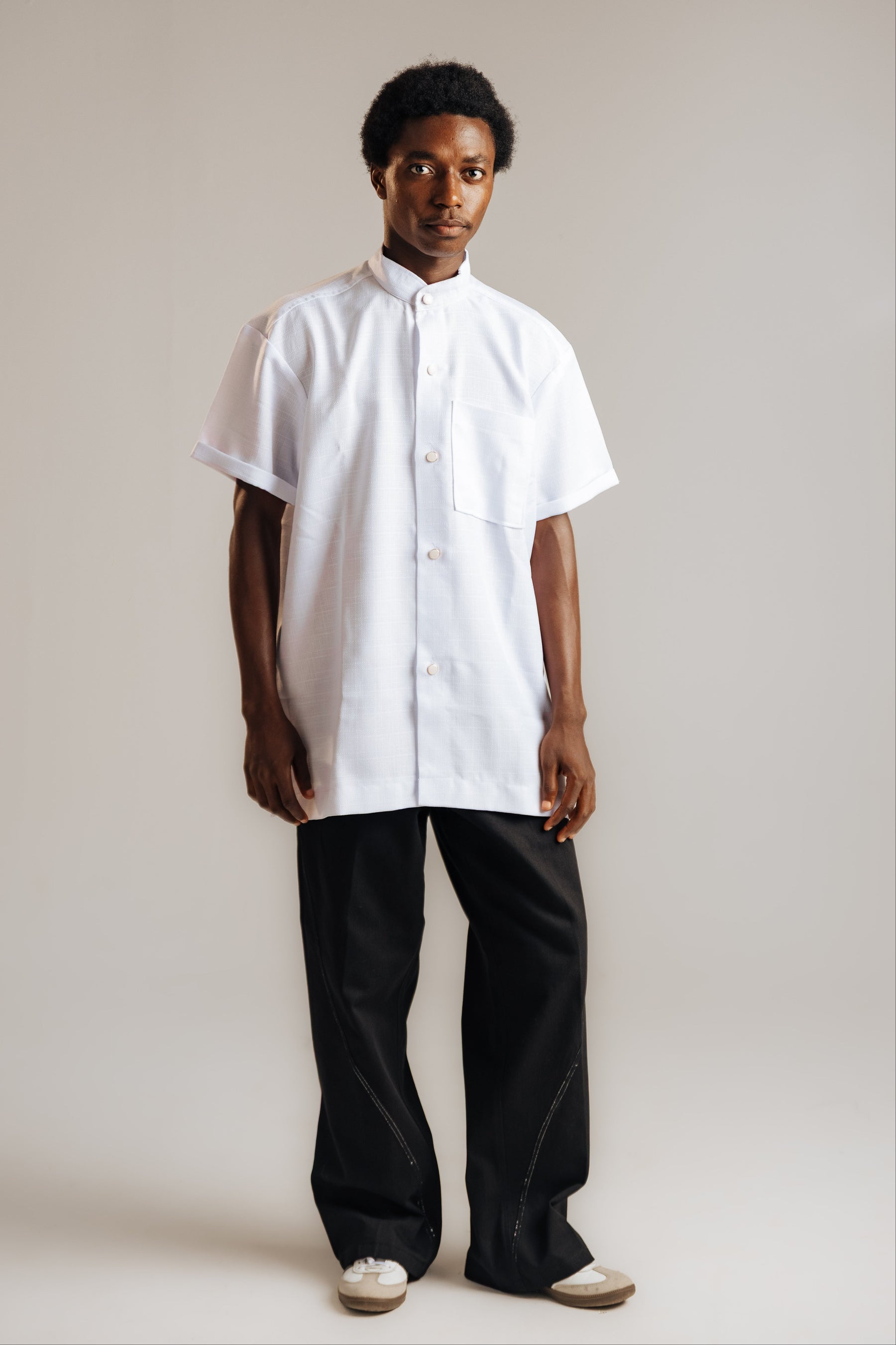 Person wearing a white shirt and black pants on a plain background