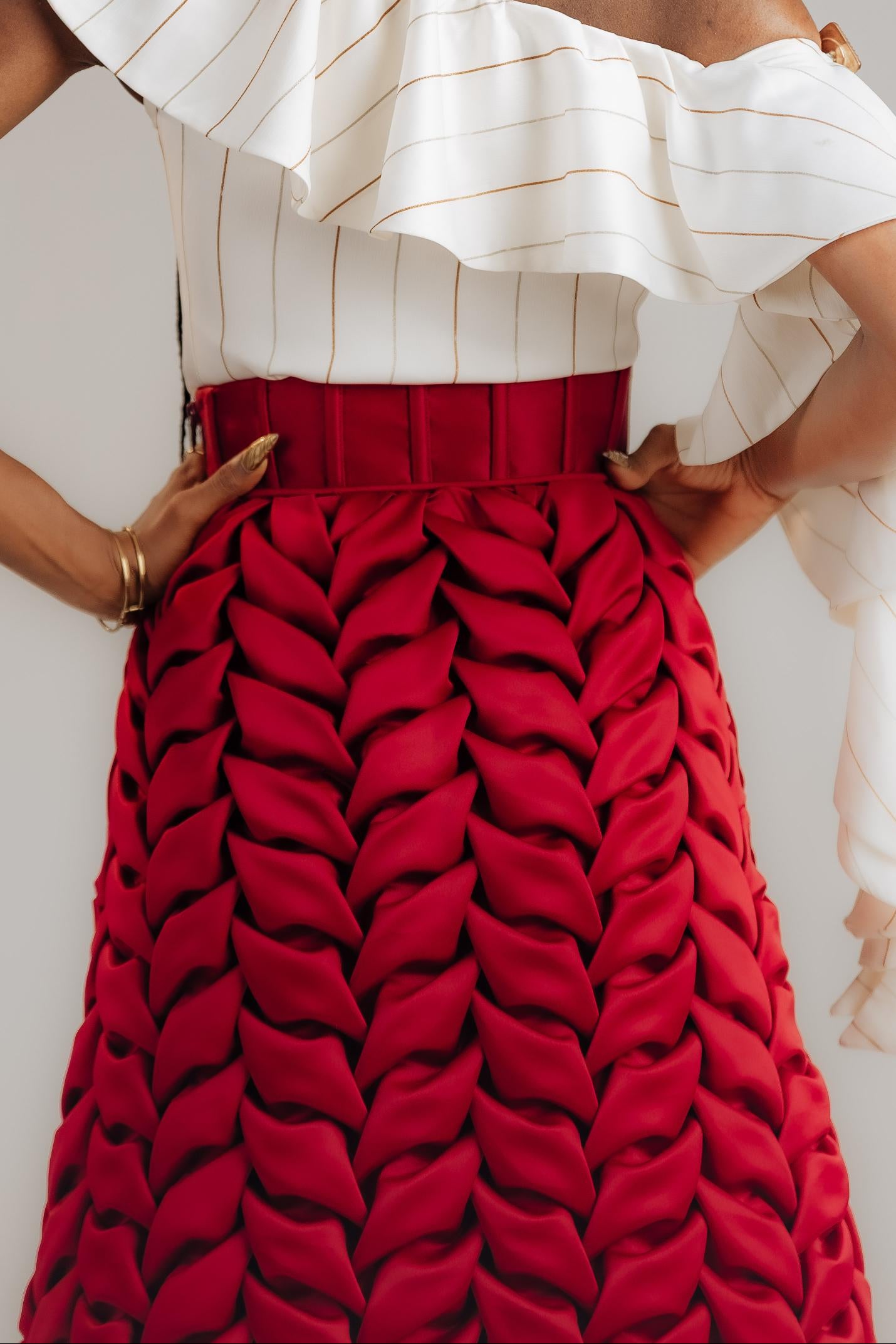 Person wearing a white off-shoulder top and red patterned skirt against a plain background