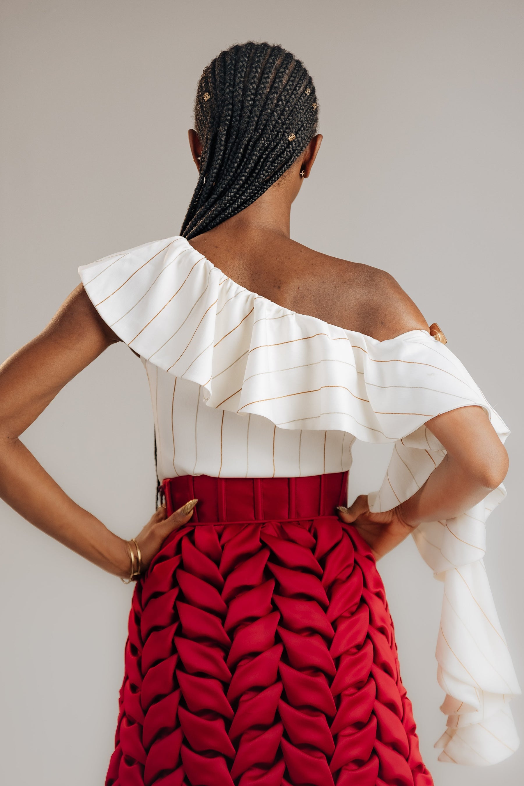 Person wearing a white off-shoulder top and red patterned skirt against a plain background