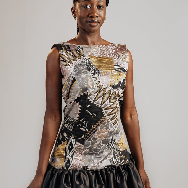 Woman wearing a sleeveless top with a floral pattern and black skirt on a plain background