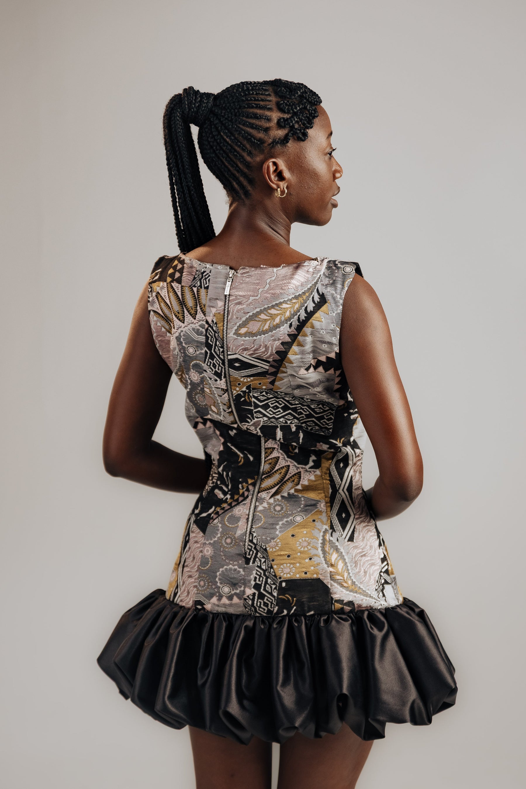 Woman wearing a patterned dress with a black skirt on a plain background